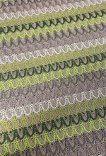 Close-up of beige and green zigzag knit jersey mesh fabric with lightweight, breathable texture for sewing and crafts