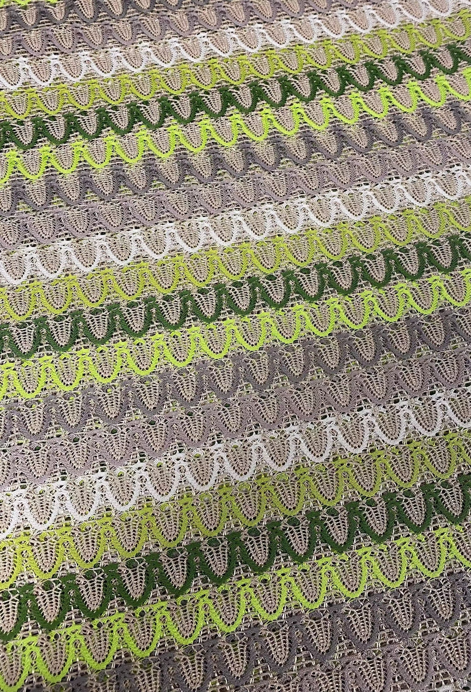Close-up of beige and green zigzag knit jersey mesh fabric with lightweight, breathable texture for sewing and crafts