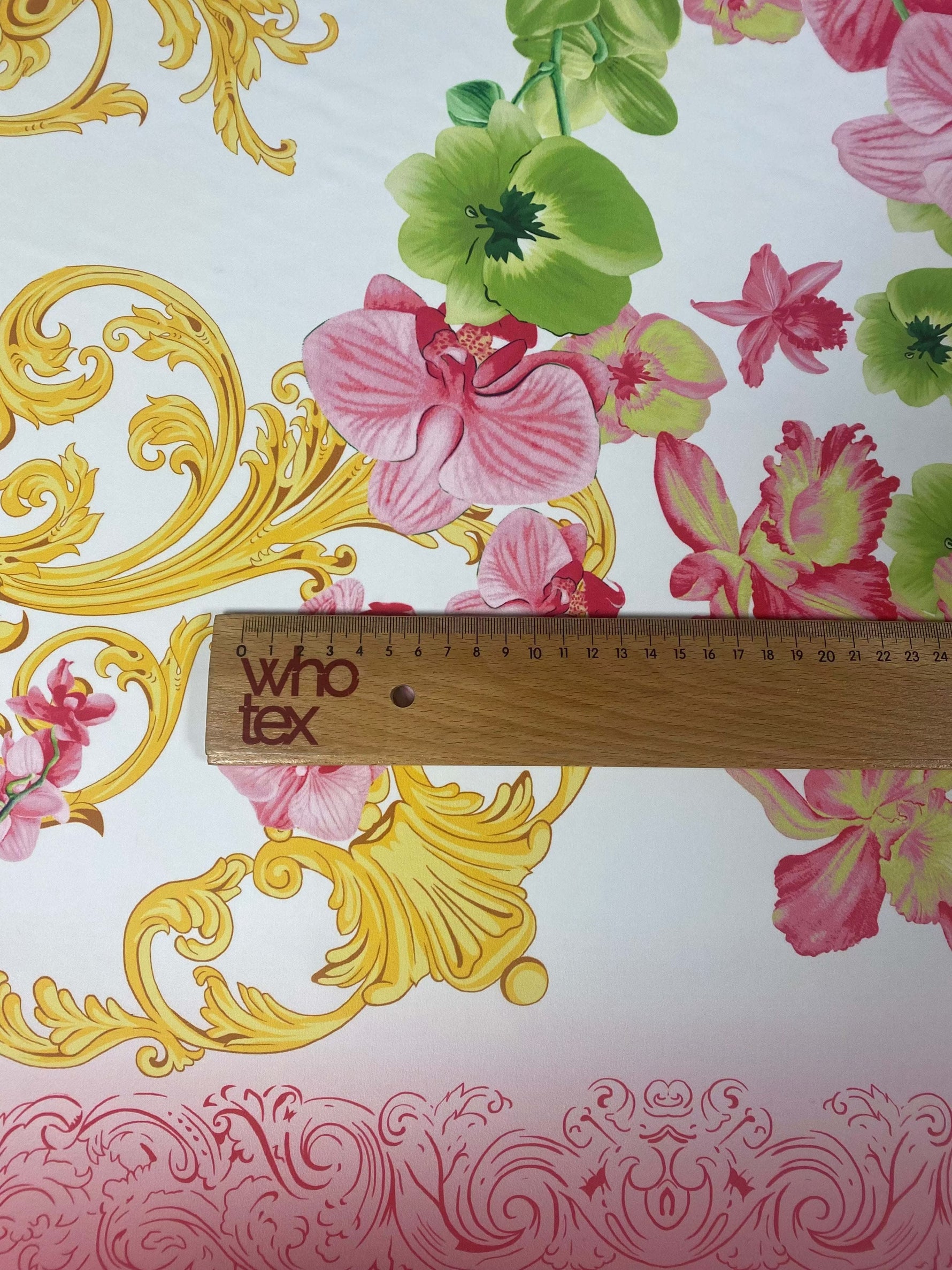 Orchid swirl print fabric with pink and green flowers and gold decorative swirls, shown with ruler for scale