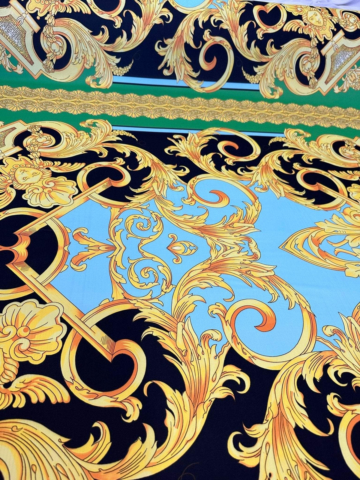 Baroque silky crepe fabric with intricate gold and black ornate patterns on blue background