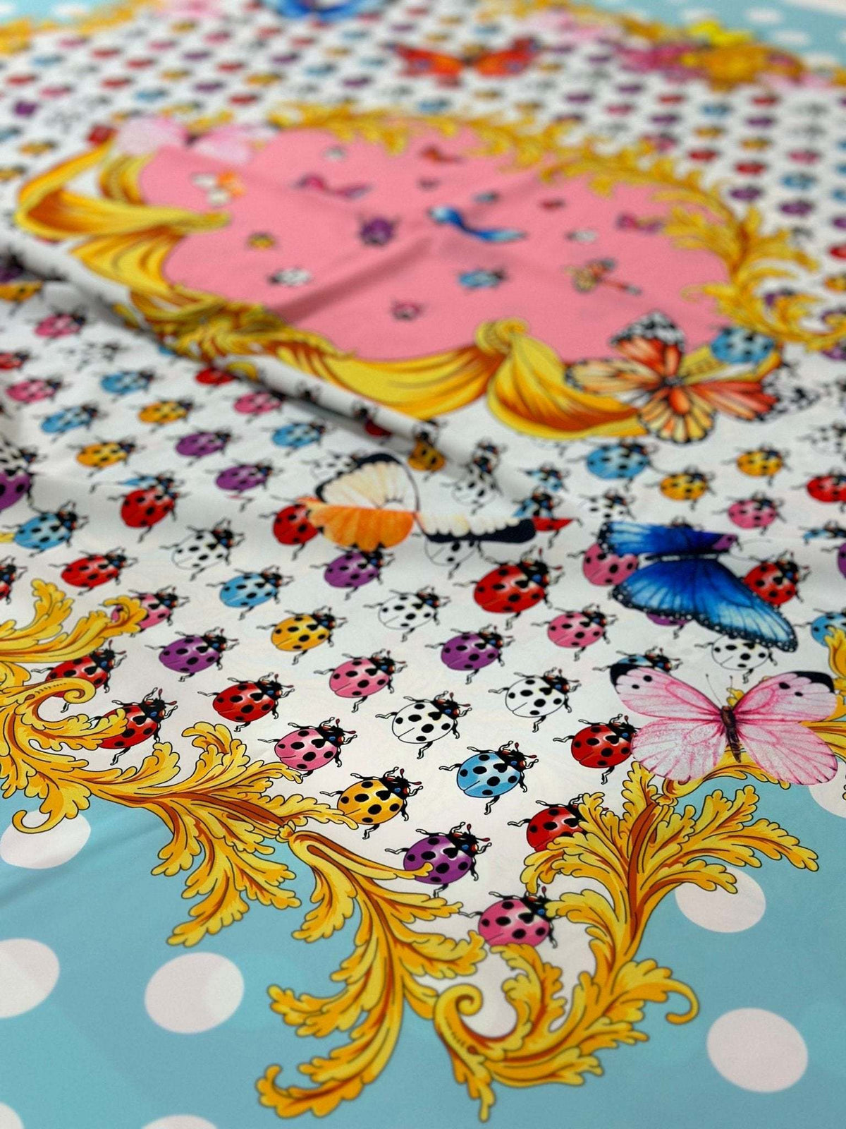 Colorful butterfly and polka dot print fabric with ladybugs and ornate golden border on light blue background