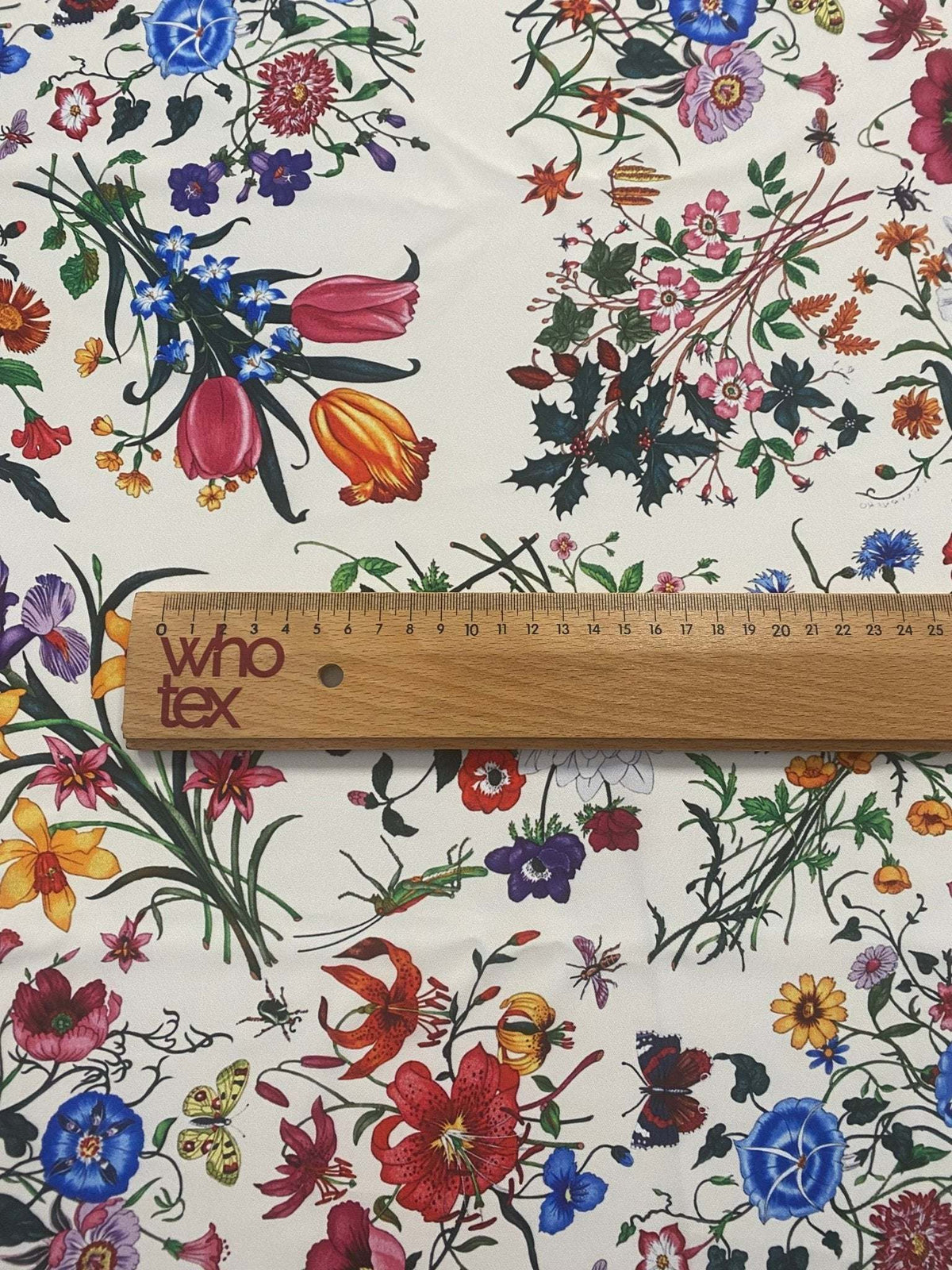 Cream floral botanical print fabric with colorful flowers on a cream background and a wooden ruler for scale