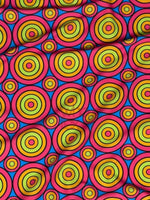 Bright colorful geometric circles print fabric with vibrant concentric ring patterns in yellow, green, blue, and red on a pink background.