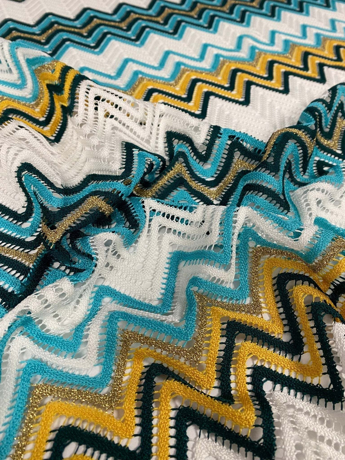 Close-up of green geometric zigzag embroidered fabric with intricate knit mesh texture for stylish garments