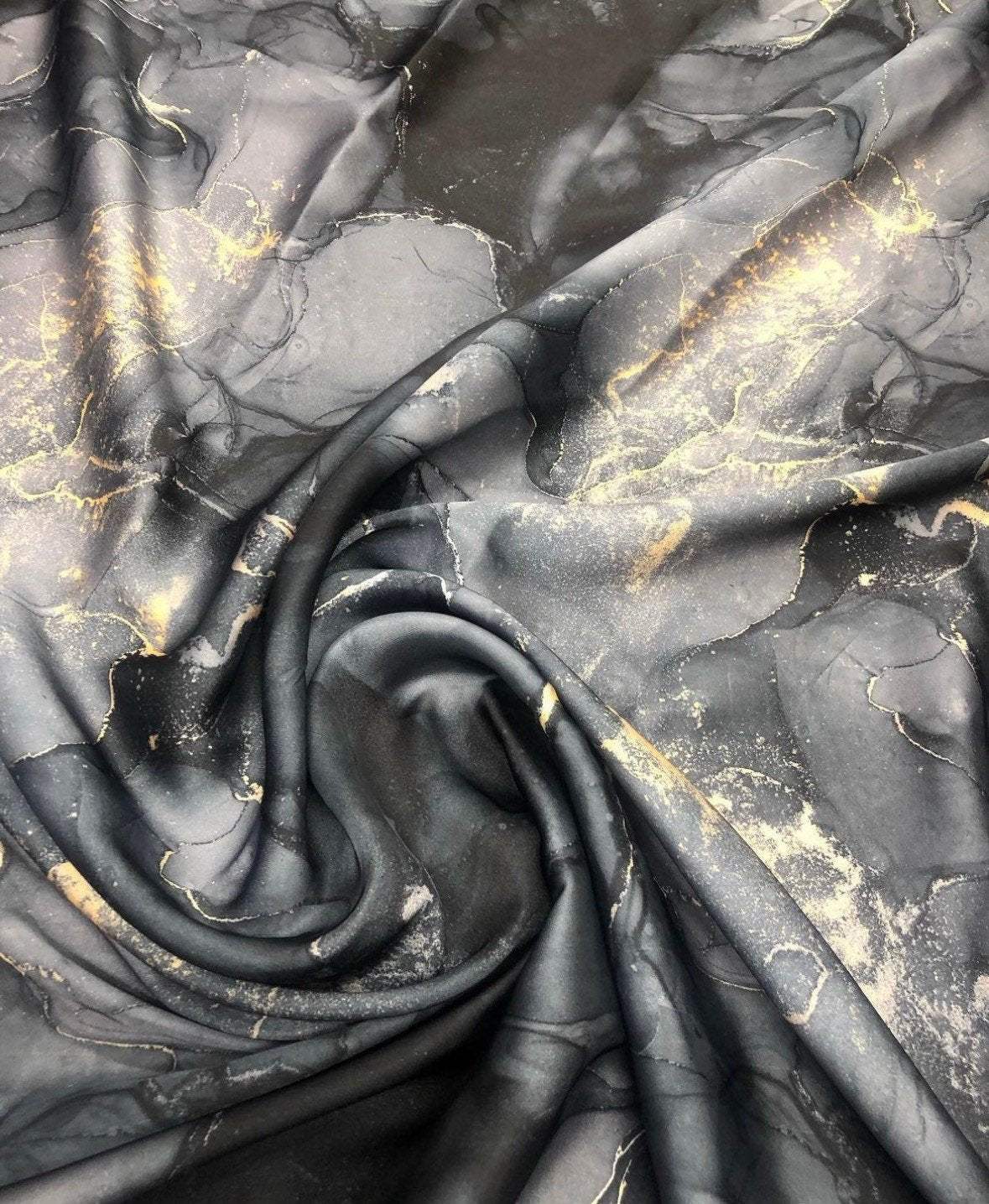 Gray tie dye fabric with gold accents in a swirling pattern, ideal for fashion and craft projects