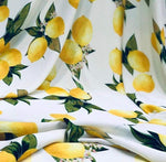 Cotton fabric with vibrant yellow lemon pattern and green leaves on white background