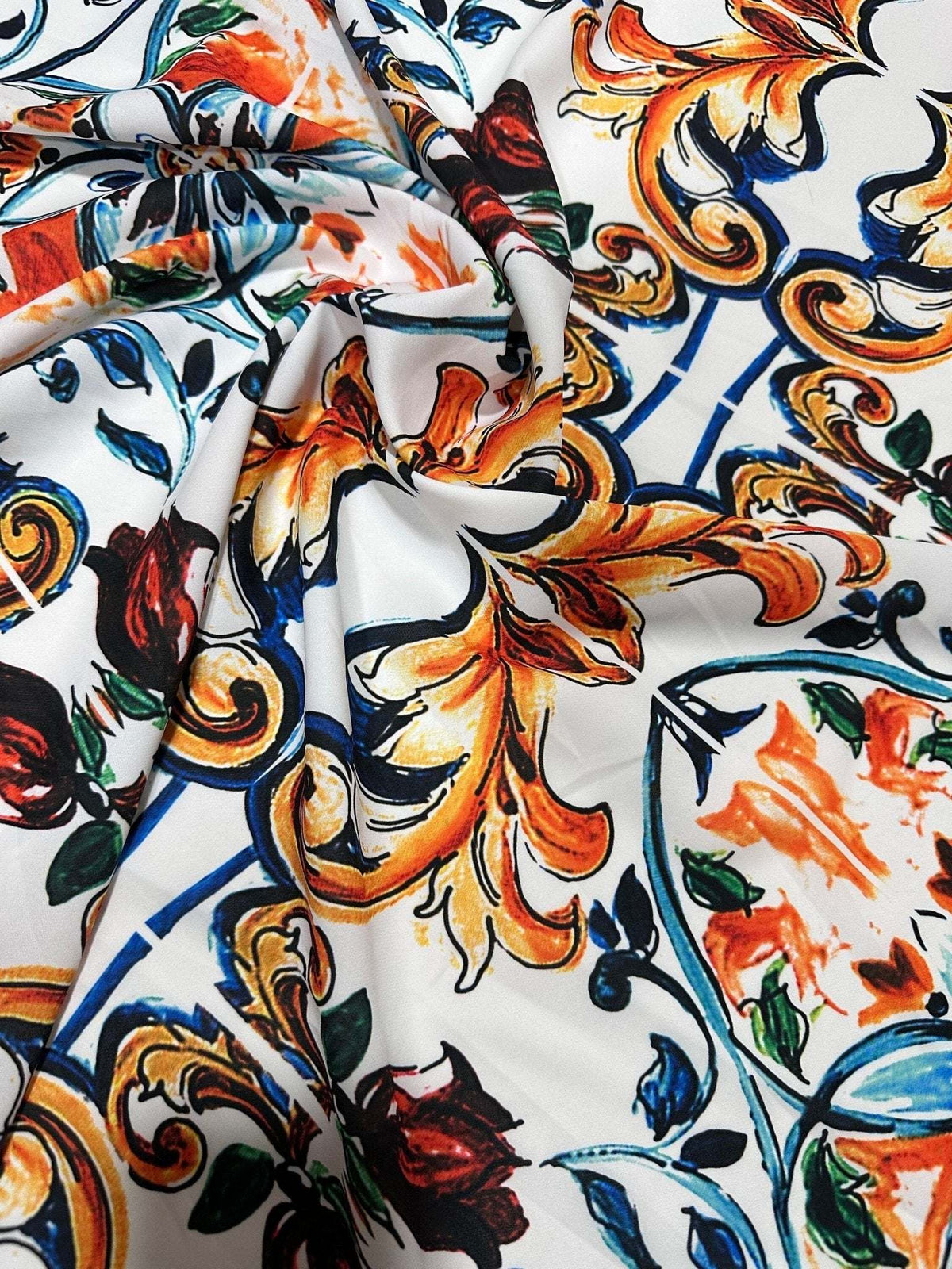 Close-up of Majolica Pattern Fabric with vibrant orange, blue, and green decorative motifs on a white background, showcasing soft and durable textile texture.