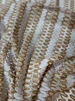 Close-up of beige and cream shimmer zigzag knit jersey fabric with chevron pattern and textured surface