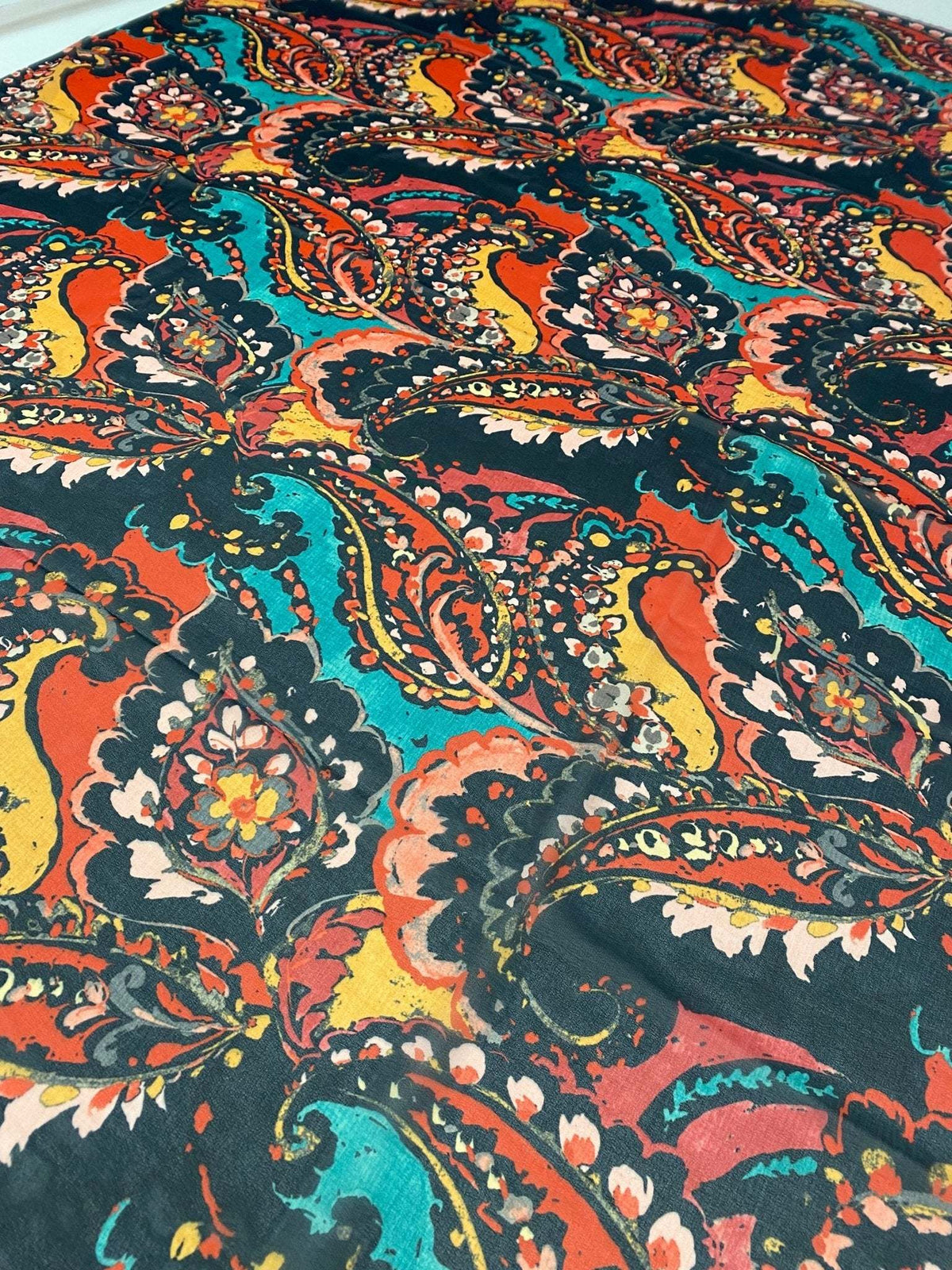 Close-up of multicolor paisley print fabric with vibrant orange, teal, and black patterns