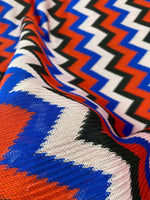Luxury zigzag knit jersey fabric with vibrant blue, red, black, and pink zigzag pattern, soft and stretchy textile for elegant garments