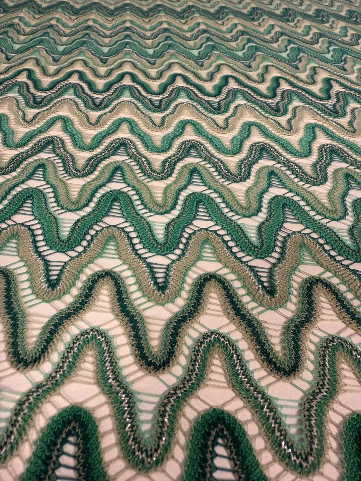 Close-up of green tones zigzag mesh fabric with textured knit pattern and open weave design